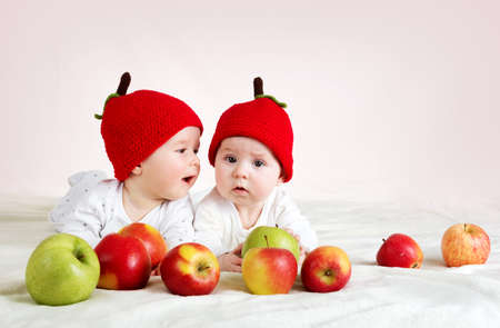 two cute six month old babies lying in hats on soft blanket with applesの写真素材