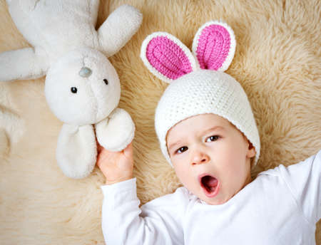 sleepy one year old baby lying in bunny hat on lamb wool backgroundの写真素材