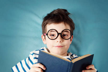 seven years old child lying with book on blue backgroundの写真素材