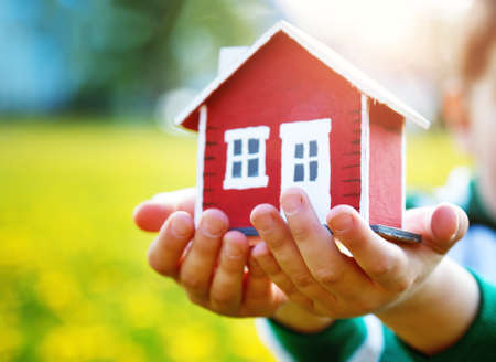 childs hands holding red wooden model houseの写真素材