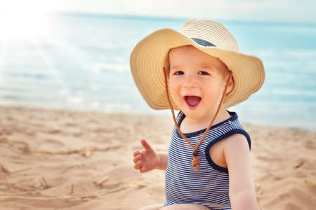 one year old boy sitting at the beach in straw hatの写真素材