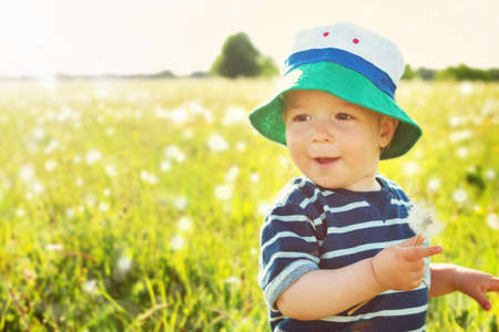 Baby boy sitting in grass on the fieald with dandelions at sunnysummer eveningの写真素材