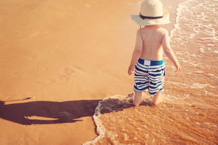 Baby boy barefoot are walking on the beach in water. Child os on vacation in summer at the seaの写真素材