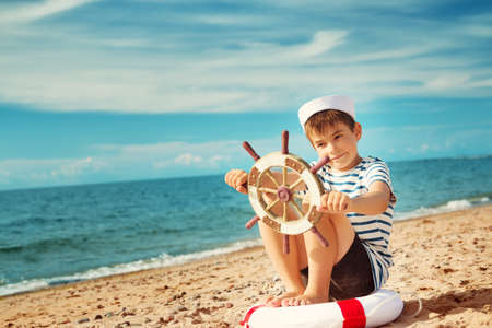 seven years old boy playing at the beach in sailor hat. Child with a steering wheel at seaの写真素材