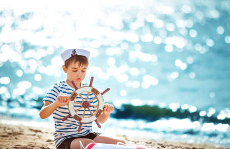 seven years old boy playing at the beach in sailor hat. Child with a steering wheel at seaの写真素材
