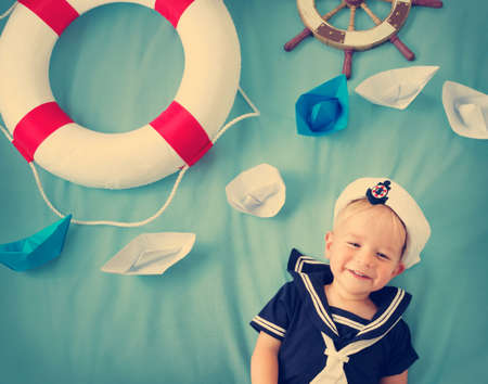 two years old boy playing in sailor hat. Child with paper ships on blue backgroundの写真素材