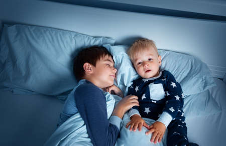 children lying in bed at night. Brothers going to sleepの写真素材