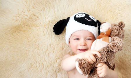 sleepy one year old baby lying in sheep hat on lamb wool backgroundの写真素材