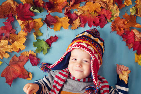 two years old boy dreaming in autumn. Child in hat and scarf and maple leaves on blue backgroundの写真素材