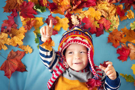 two years old boy dreaming in autumn. Child in hat and scarf playing with maple leaves on blue backgroundの写真素材