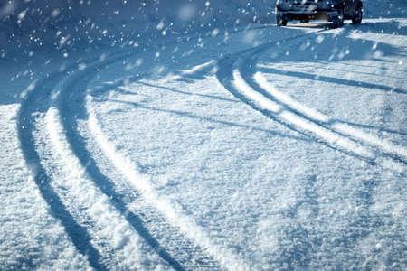 Car tires on winter road covered with snow. Vehicle on snowy alley in the morning at snowfallの写真素材