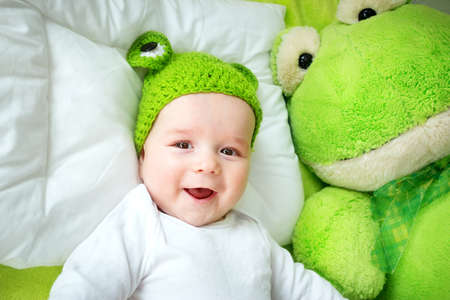 little boy in knitted animal hat lying on soft green blanket with frog softtoy. Cute 5 month old baby on the pillow in bedの写真素材