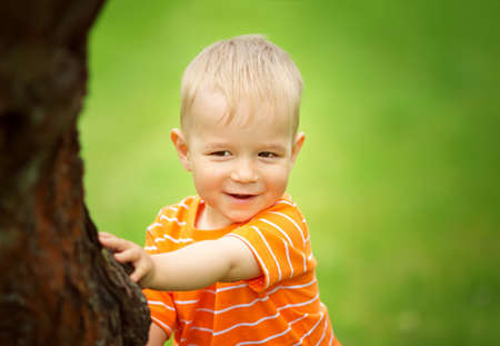 Happy little boy playing in the garden. Child hiding under tree in summerの写真素材
