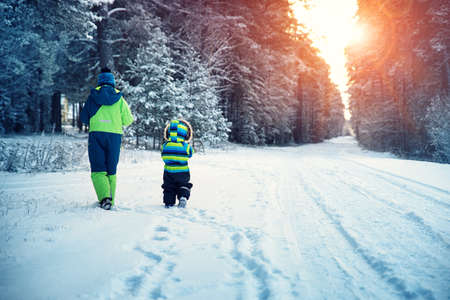Children walking on snow at snowfall. Boys in winter clothes outdoors in cold weatherの写真素材
