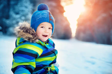 Baby boy walking at snowfall. Child in winter clothes playing with snowの写真素材