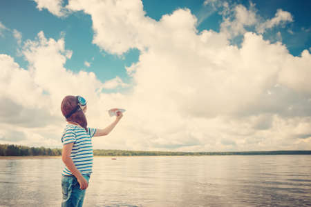 boy playing with a paper plane in aviator hatの写真素材