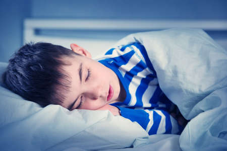 Boy sleeping in bed in pajamasの写真素材