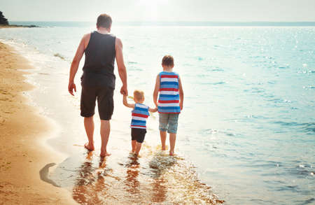 Father and sons walking at the beach at seaの写真素材