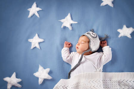 Cute newborn baby girl lying in the bed. 2 month old child in owl hat sleeping on blue blanket