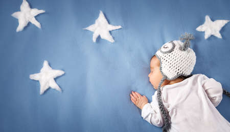 Cute newborn baby girl lying in the bed. 2 month old child in owl hat sleeping on blue blanketの写真素材