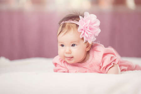 Cute little baby girl lying in the bed in pink dressの写真素材