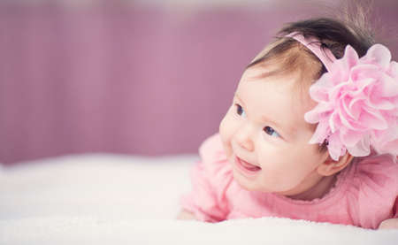 Cute little baby girl lying in the bed in pink dressの写真素材