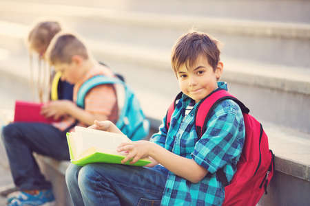 Children with rucksacks sitting on the stairs near schoolの写真素材