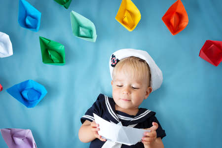 A boy playing in sailor hat with paper ships on blueの写真素材