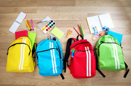 Colourful children schoolbags on wooden floor. Backpacks with school accessoriesの写真素材
