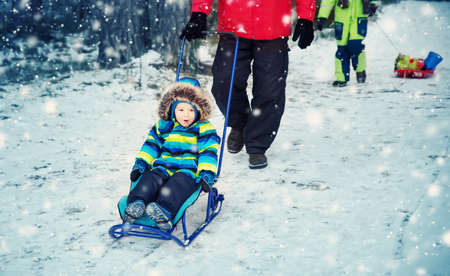 Father with sons walking at snowfallの写真素材