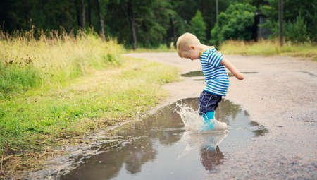Child walking in wellies in puddle on rainy weatherの写真素材