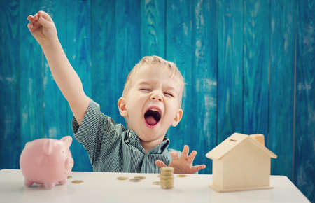 two years old child sitting on the floor and putting a coin into a piggybankの写真素材