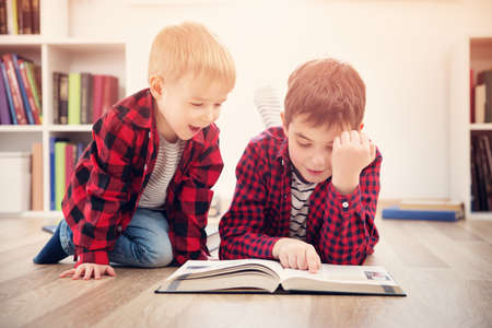 Three years old child and his older brother sitting among books at homeの写真素材
