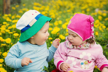 Little boy and girl in hats sitting on the field with soft toys in summerの写真素材