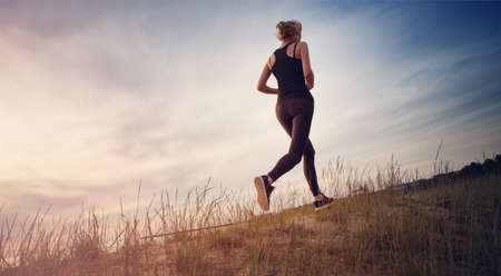 Young woman running on the field near seaside at sunsetの写真素材