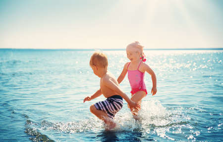 Boy and girl playing on the beach on summer holidays. Children in nature with beautiful sea, sand and blue sky. Happy kids on vacations at seaside running in the waterの写真素材