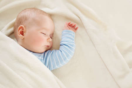 Baby sleeping covered with soft white blanketの写真素材
