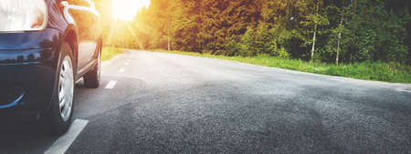 Car on asphalt road on summer day at park. Transportation panoramic background with sunlightの写真素材