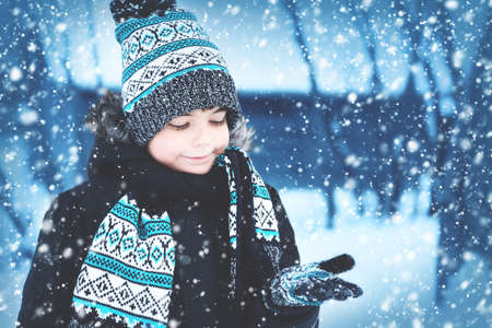 Boy in knitted hat, gloves and scarf outdoors at snowfallの写真素材