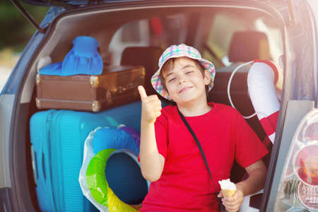 child sitting in car filled with traveling accessoriesの写真素材
