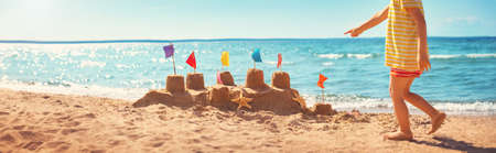 boy building a sandcastle at the beach in summer. Child on vacations at blue sea playing in sand near water and having funの写真素材