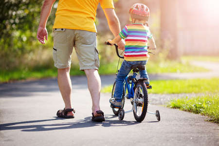 a child on a bicycle in helmet with father on asphalt roadの写真素材