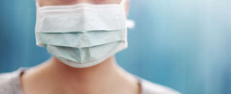 young woman in medical face protection mask indoors on blue background. Sick personの写真素材
