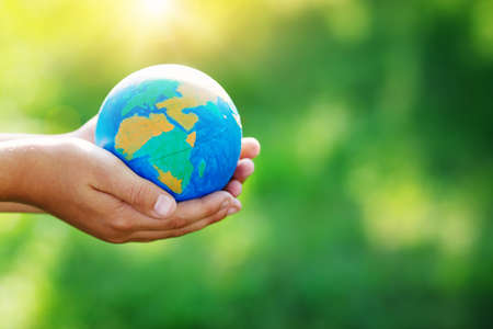 Hands of a child taking care of planet earth. Handmade painted globe on sunny day in the garden in summerの写真素材