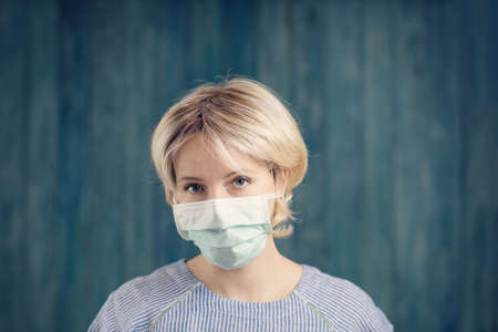 young woman in medical face protection mask indoors on blue background