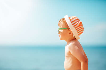 little boy smiling at the beach in hat with sunglassesの写真素材