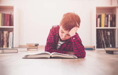 Eight years old child lying on the floor among books at homeの写真素材