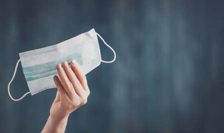 young woman holding face protection mask indoors on blue background.の写真素材