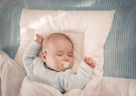 Baby sleeping covered with soft white blanketの写真素材