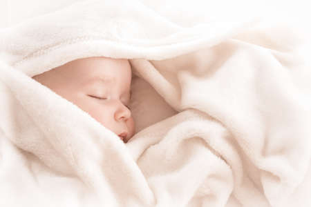 Baby sleeping covered with soft white blanketの写真素材